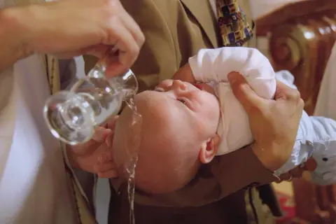 Un bébé est baptisé, l'eau bénite coule sur sa tête. Un moment solennel pour comprendre pourquoi baptiser son enfant.