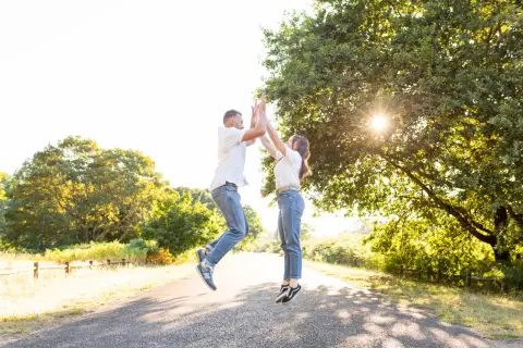 Un couple saute de joie sur un chemin ensoleillé, une belle photo d'engagement dans la nature.