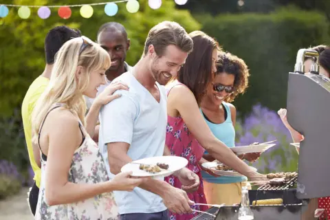 Des amis profitent d'un barbecue pour mariage en plein air, avec des brochettes et du maïs grillé.