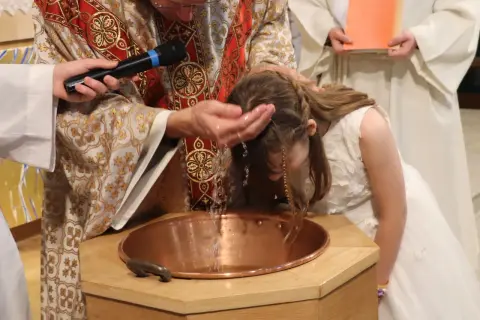 Cérémonie de baptême d'enfants : un prêtre verse de l'eau sur la tête d'une jeune fille dans une église.