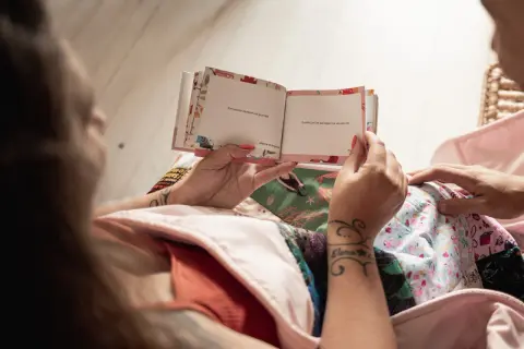 Un livre ouvert avec des messages tendres, comme un texte pour mon filleul. Les mains tiennent le livre, entourées de tissus colorés.