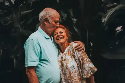 Un couple âgé s'embrasse tendrement, un moment de joie pour fêter sa retraite en famille.