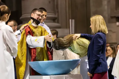 Cérémonie de baptiser en arabe. Un prêtre verse de l'eau sur la tête d'une femme dans un bassin bleu.