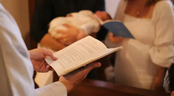 Célébration d'un baptême : un livre ouvert est tenu, un bébé est porté, et des parents écoutent attentivement la bénédiction.