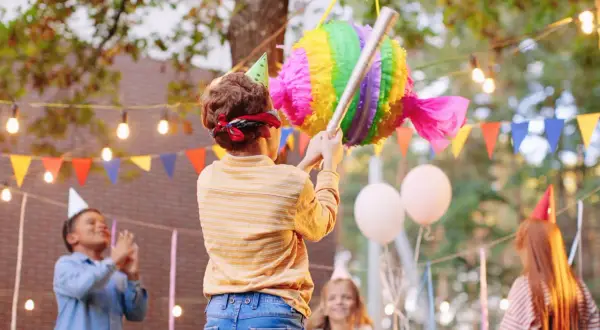 Enfants en fête, un garçon bandeau sur les yeux s'apprête à frapper une pinata colorée. L'art de fabriquer une pinata pour un joyeux anniversaire.