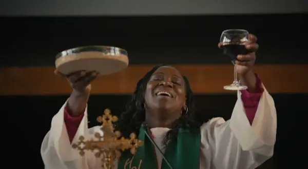 Une femme, peut-être une marraine de substitution, célèbre la communion en levant une coupe de vin et une patène.