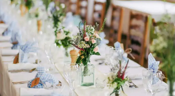 Décoration baptême champêtre à faire soi-même : table dressée avec nappes blanches, bouquets de fleurs sauvages, serviettes à carreaux bleus et bois.