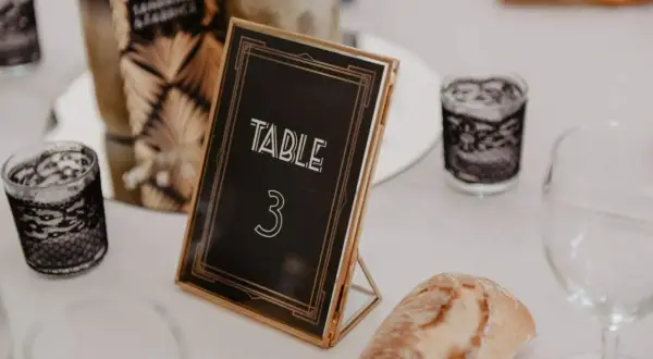 Un nom de table mariage chic, "TABLE 3", dans un cadre doré, entouré de bougies décoratives et d'une tranche de pain.
