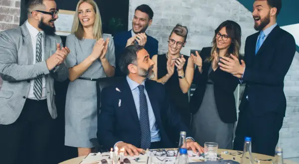 Une équipe célèbre le départ à la retraite de son collègue avec un gâteau et des applaudissements. Un texte invitation départ retraite humoristique serait parfait pour cette occasion !