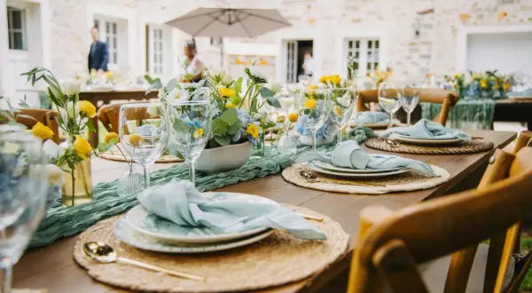 Table dressée pour un thème anniversaire adulte, avec des fleurs bleues et jaunes, des serviettes bleu pâle et des couverts dorés.