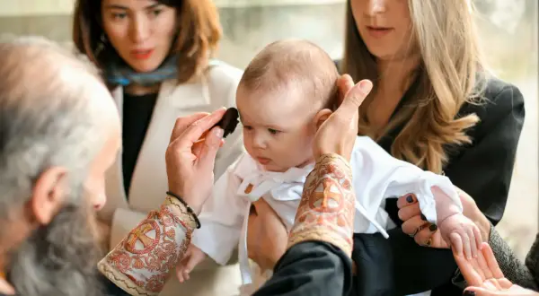 Cérémonie religieuse : un bébé est tenu par sa marraine. Le prêtre applique une onction. Peut-on changer de marraine ?