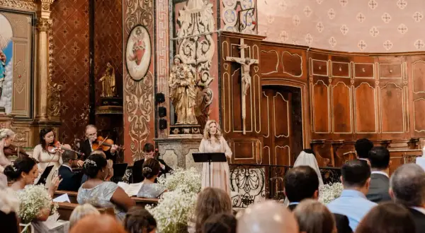 Une femme chante lors d'un mariage, accompagnée d'un orchestre. La prière universelle du mariage résonne dans l'église ornée.