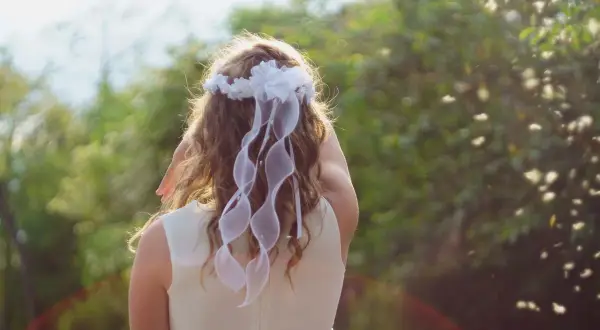 Coiffure fille communion : une jolie tresse ornée d'un diadème de fleurs blanches et de rubans flottants, prête pour sa grande journée.