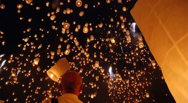 Un homme observe une multitude de lanternes thaïlandaises illuminant le ciel nocturne, créant un spectacle magique.
