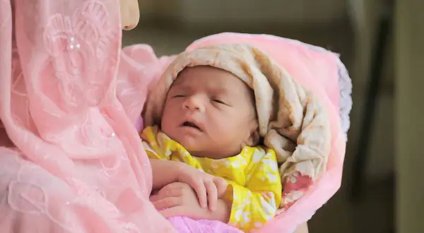 Une mère câline son nouveau-né, enveloppé dans des tissus roses et crème. Une douce image pour des douces félicitations naissance islam.