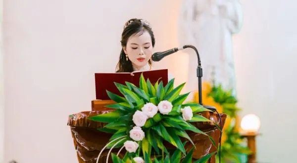 Une femme lit un texte devant un pupitre fleuri. La question "faut il etre baptisé pour etre temoin a l'eglise" résonne.
