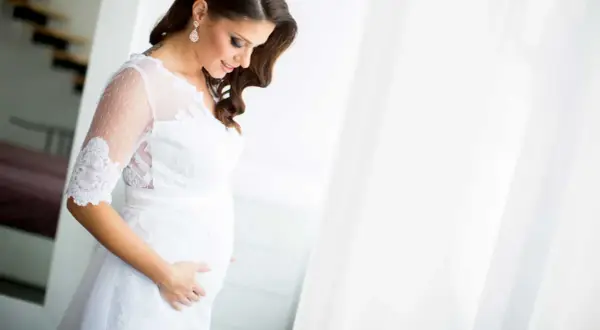 Une future mariée enceinte, vêtue d'une robe blanche, caresse son ventre avec tendresse.