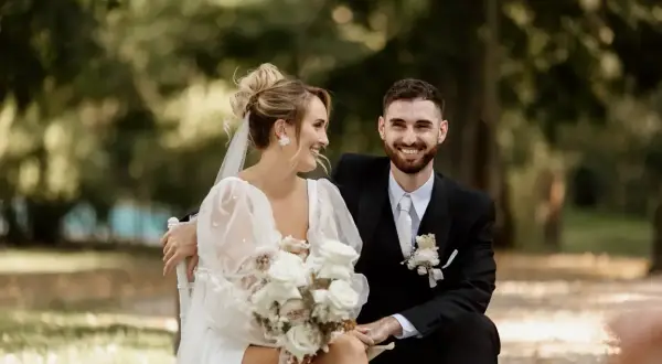 Un couple rayonnant, le marié en costume noir, la mariée en robe blanche, échangeant des regards complices lors de leur échange de voeux mariage.