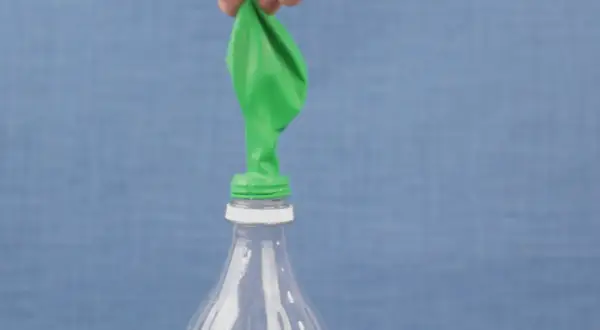 Un ballon vert est posé sur le goulot d'une bouteille en plastique. Une main le tient, prêt à montrer comment gonfler un ballon.