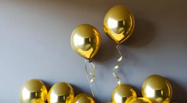 Des ballons dorés brillants flottent près d'un mur. Une astuce pour savoir comment faire tenir des ballons au plafond : utilisez du ruban adhésif double face.