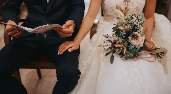 Un couple se tient la main, le marié lit un document, la mariée tient un bouquet. La musique de la sortie de mairie résonne.