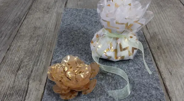 Un sachet dragees a faire soi meme, décoré de motifs dorés, à côté d'une fleur en papier.