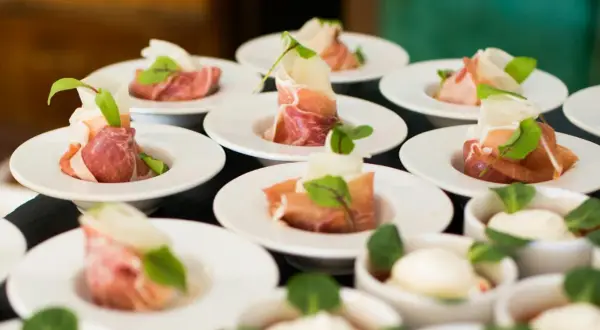 Petits amuse-bouches de jambon cru roulé, melon et garniture verte, prêts pour un dîner assis.