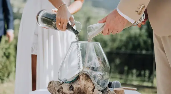 Un couple unit ses vies lors d'une cérémonie du sable, versant ensemble du sable de deux récipients dans un vase, symbolisant leur union.