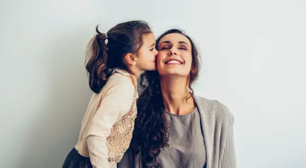 Une petite fille embrasse sa mère sur la joue. Elle pense : "je ne sais pas qui choisir comme marraine", mais l'amour est évident.