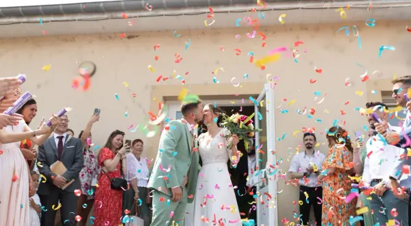Un couple s'embrasse sous une pluie de confettis colorés, formant une haie d'honneur mariage joyeuse.