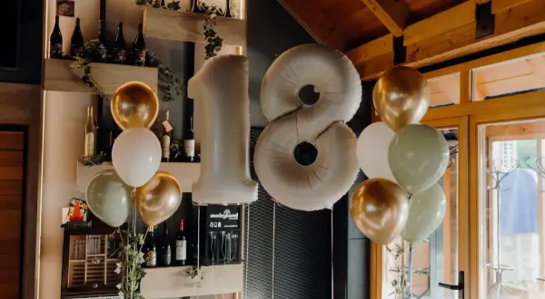 Ballons dorés, blancs et verts flottent près d'un grand ballon chiffre 18, parfait pour une fête d'anniversaire.