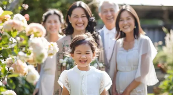 Une famille souriante célèbre un baptême laïque dans un jardin fleuri. La petite fille au premier plan rayonne de joie.