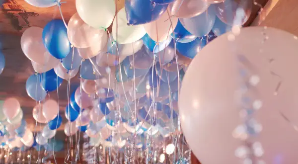 Une multitude de ballons bleus, blancs et roses flottent au plafond, prêts à gonfler avec de l'hélium pour une fête.