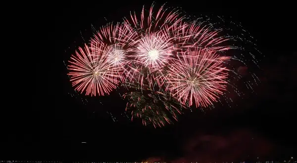 Un spectaculaire feu d'artifice illumine le ciel nocturne au-dessus de l'eau, reflétant ses couleurs vives sur la surface calme.