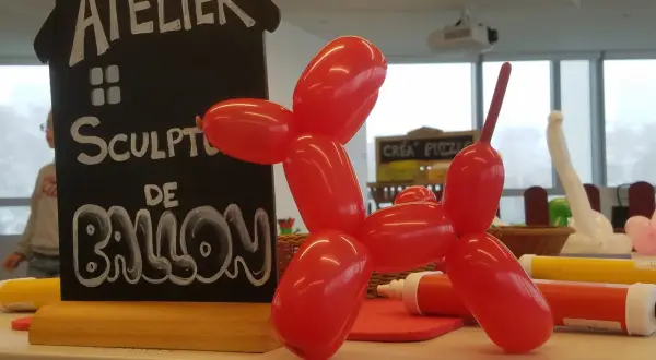 Un chien en sculpture ballon rouge, à côté d'un panneau "Atelier Sculpture de Ballon". Facile à réaliser !