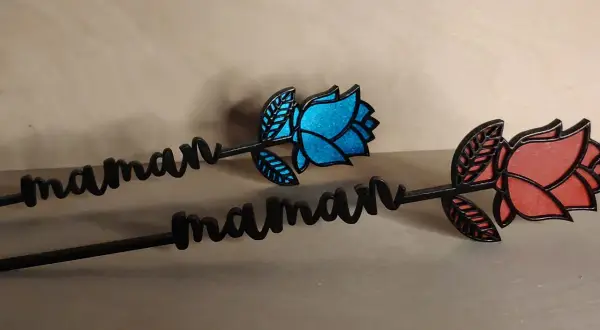 Deux roses décoratives avec le prénom "maman" gravé, l'une bleue, l'autre rouge.