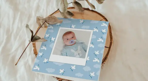 Carte de baptême originale pour un garçon, avec une photo de bébé sur fond bleu ciel orné de colombes et de nuages.