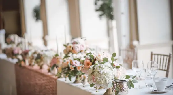 Magnifique centre de table floral pour un mariage, avec des roses pâles et des hortensias blancs. Une bougie mariage subtile complète la scène.