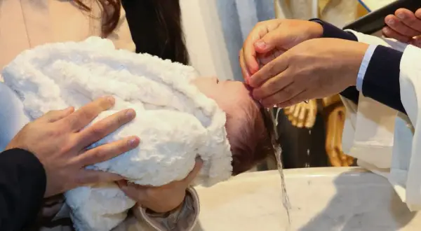 Cérémonie de baptême en hiver. Un bébé est tenu par ses parents, une main verse de l'eau sur sa tête.