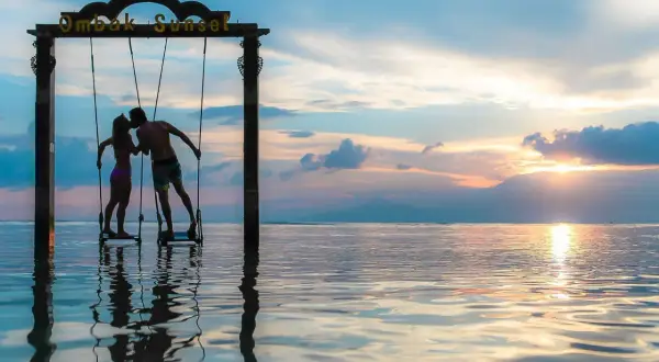 Couple s'embrassant sur des balançoires au coucher du soleil, une parfaite destination lune de miel pas cher.