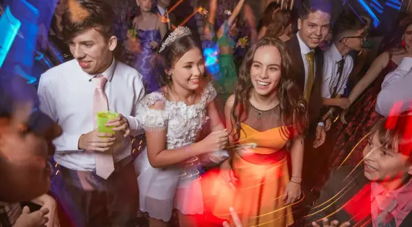 Des jeunes gens s'amusent lors d'une soirée bal, riant et dansant sous les lumières vives.