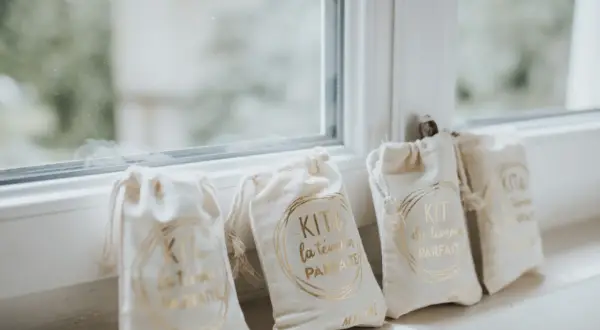 Quatre petits sacs en tissu écru, chacun portant l'inscription dorée "KIT du témoin PARFAIT". Un cadeau témoin mariage personnalisé, prêt à être offert.