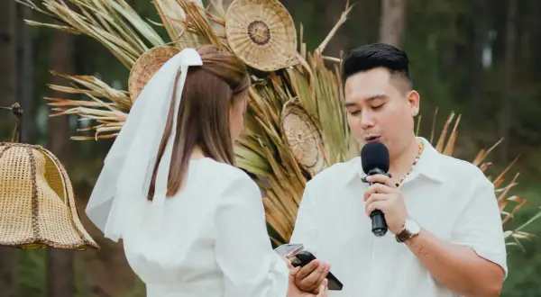 Un homme prononce un discours de mariage devant une femme voilée, micro en main, lors d'une cérémonie en plein air.