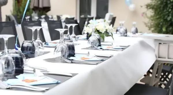 Table dressée pour une fête de baptême, avec des verres, des couverts et des décorations bleues.