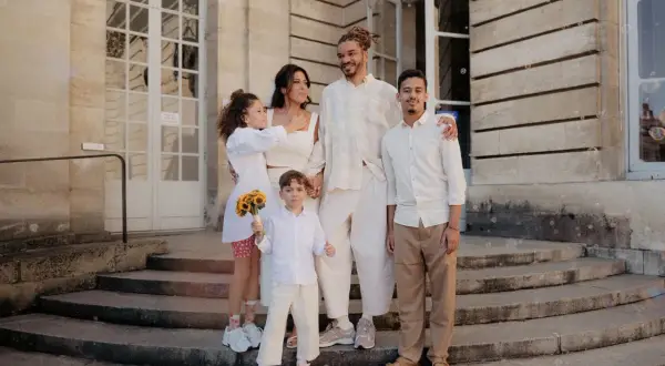 Famille réunie devant un bâtiment, le couple marié entouré de leurs enfants. La plus jeune porte un bouquet de tournesols, un vrai témoin mariage.