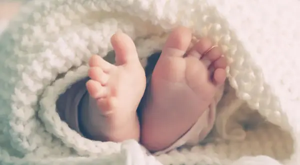 Les petits pieds d'un bébé, enveloppés dans une couverture douce, symbolisant le rôle de parrain/marraine après le décès des parents.