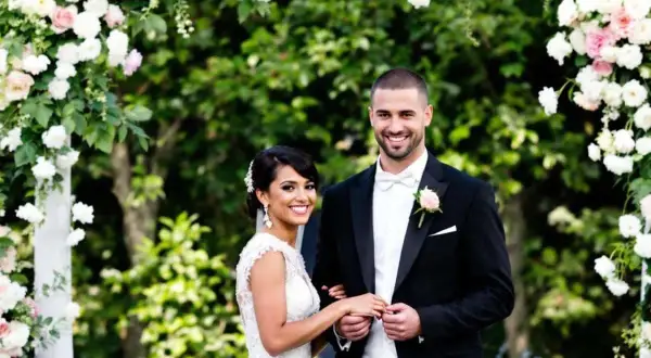 Un couple souriant, paré pour leur cérémonie d'engagement mariage, sous une arche fleurie.