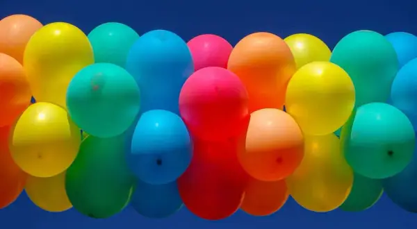 Un amas de ballons colorés flottant dans un ciel bleu. Combien de temps tient un ballon gonflé à l'air ? Cela dépend de sa taille et du matériau.