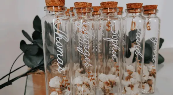 Bouteilles en verre avec fleurs séchées, bouchons en liège et breloques dorées. Parfait cadeau invité bapteme diy personnalisé avec des prénoms.