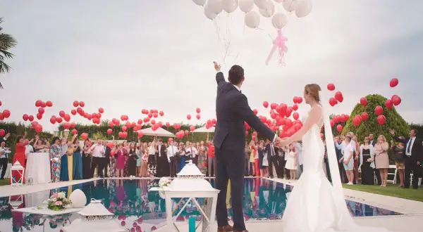 Mariés lançant des ballons rouges et blancs lors d'une animation mariage, avec des invités autour d'une piscine.